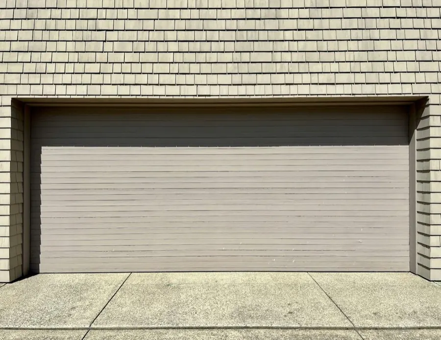 Close-up of a full-width grey sectional garage door beneath shake siding